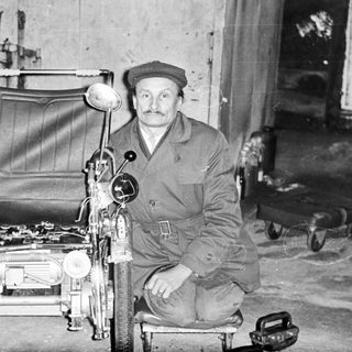 Man poses with a unique, homemade vehicle in a workshop.