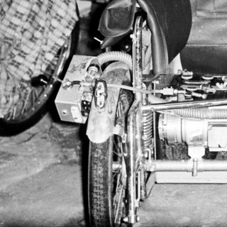 Man poses with a unique, homemade vehicle in a workshop.