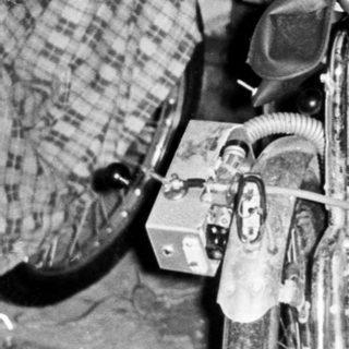 Man seated next to a vintage three-wheeled vehicle.