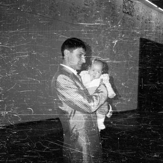 Man in suit holds baby in a dimly lit space.