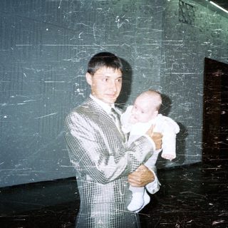 Man in suit holds baby in a stark, industrial space.
