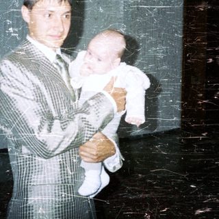 Man in suit holds baby in a stark, industrial space.
