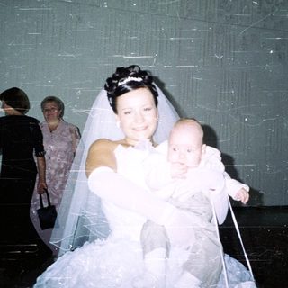 Bride holding baby, with guests in the background.