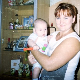 Here's a brief summary of the image: Woman holding baby in a room with shelves.