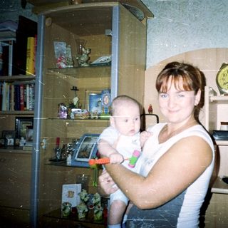 Here's a brief summary of the image: Woman holding baby in a room with shelves.