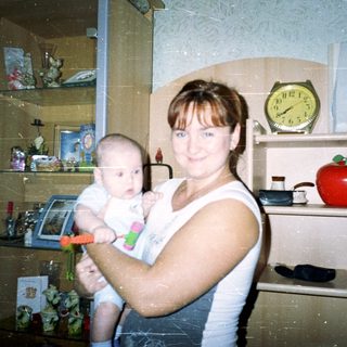 Here's a brief summary of the image: Woman holding baby in a room with shelves.