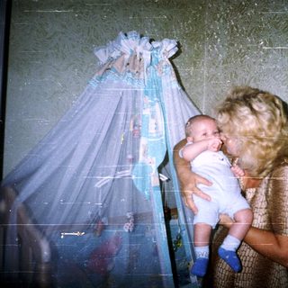 Mother holds baby, standing near a crib.