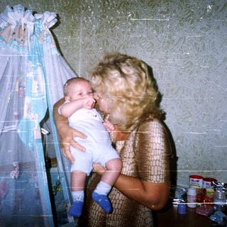 Mother holds baby, standing near a crib.