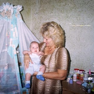 Woman holding a baby in a bedroom with a playpen.