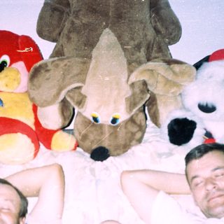 Men and baby sleep under large stuffed animals.