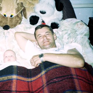 Men and a baby relax on a bed with toys.