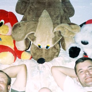 Men and a baby relax on a bed with toys.