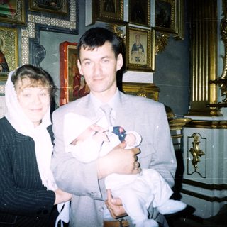 Couple holds newborn baby in an ornate church setting.
