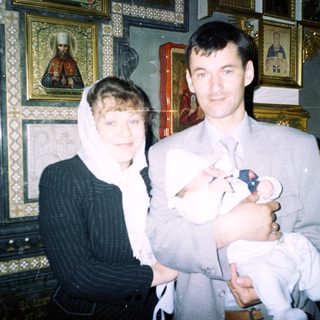 Couple holds newborn baby in an ornate church setting.
