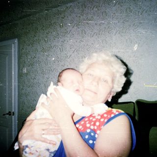 Elderly woman holding a newborn baby indoors.