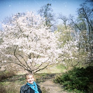 Woman stands near a blossoming tree in a park.