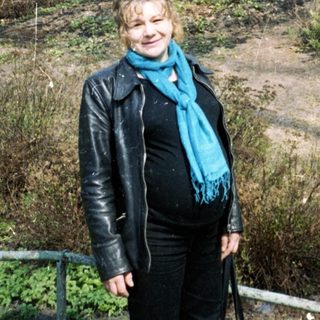 Woman stands near a blossoming tree in a park.