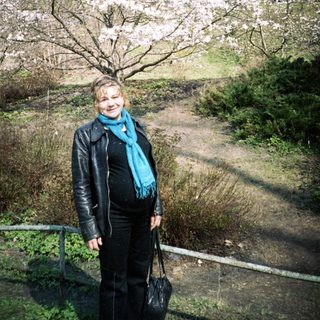 Woman stands near a blossoming tree in a park.