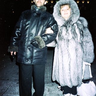 Couple stands outdoors in winter clothing, appearing stylish.