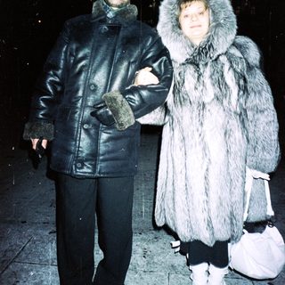 Couple stands outdoors in winter clothing, appearing stylish.