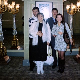 Four people pose indoors near ornate, decorative candelabras.
