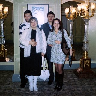 Four people pose indoors near ornate, decorative candelabras.