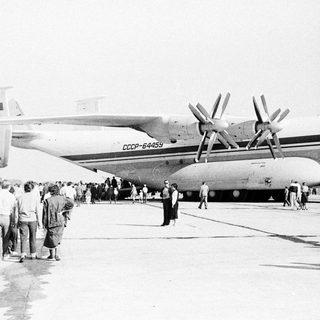 Soviet Antonov An-12 transport plane on tarmac, crowd watching.