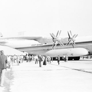 Crowd gathers near a Soviet-era airplane on an airfield.