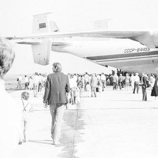 Crowd gathers near a Soviet-era airplane on an airfield.