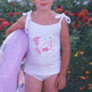 Girl in swimsuit stands near flowers, holding an inflatable ring.