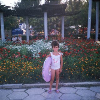 Girl in swimsuit stands near flowers, holding an inflatable ring.