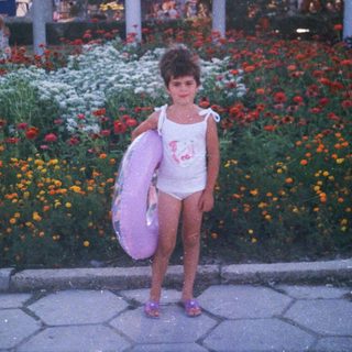 Girl in swimsuit stands near flowers, holding an inflatable ring.