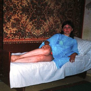 Woman in blue gown lies on a bed in a room.