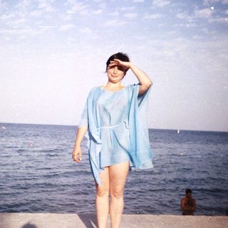 Woman in blue dress stands on a pier overlooking the sea.