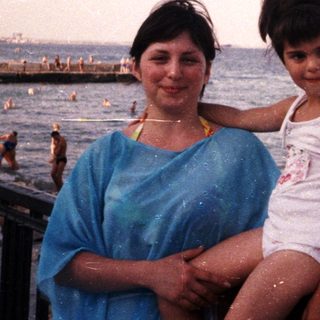 Woman and child pose by the beach, ocean backdrop.