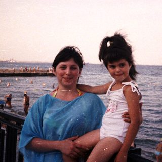 Woman and child pose by the beach, ocean backdrop.