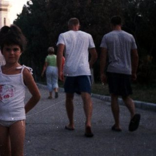 Girl stands on road with group of people nearby.