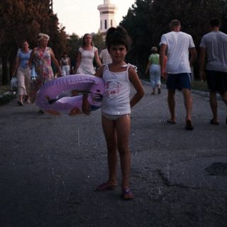 Girl stands on road with group of people nearby.