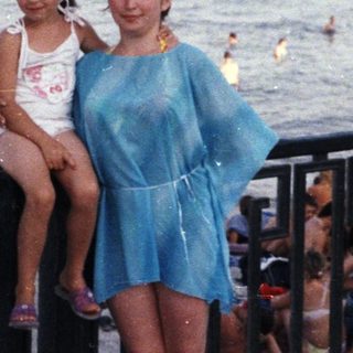 Woman and child pose by the sea, looking towards a port.
