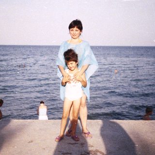 A woman and child stand on a concrete edge by the sea.