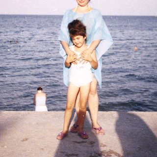 A woman and child stand on a concrete edge by the sea.