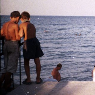 A woman and child stand on a concrete edge by the sea.