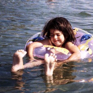 Child floats in a crowded beach, enjoying the water.