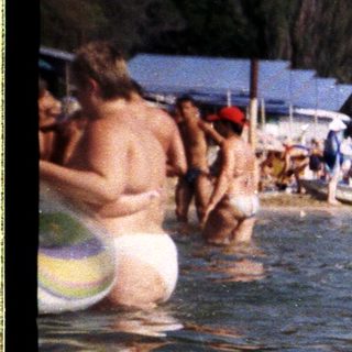 Child floats in a crowded beach, enjoying the water.