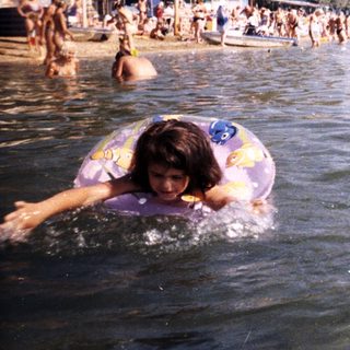 Girl swims in a crowded lake with a floatie.