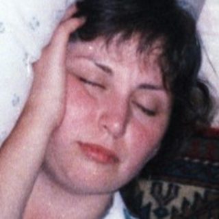 Here's a brief summary: Woman lying on a bed, partially visible in a room.