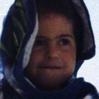 Person wrapped in towel, standing on a crowded beach.