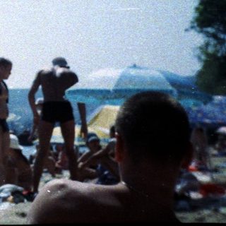 Person wrapped in towel, standing on a crowded beach.
