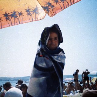 Person wrapped in towel, standing on a crowded beach.
