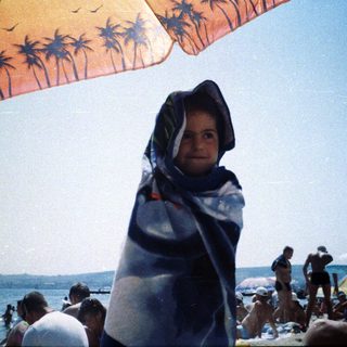 Person wrapped in towel, standing on a crowded beach.